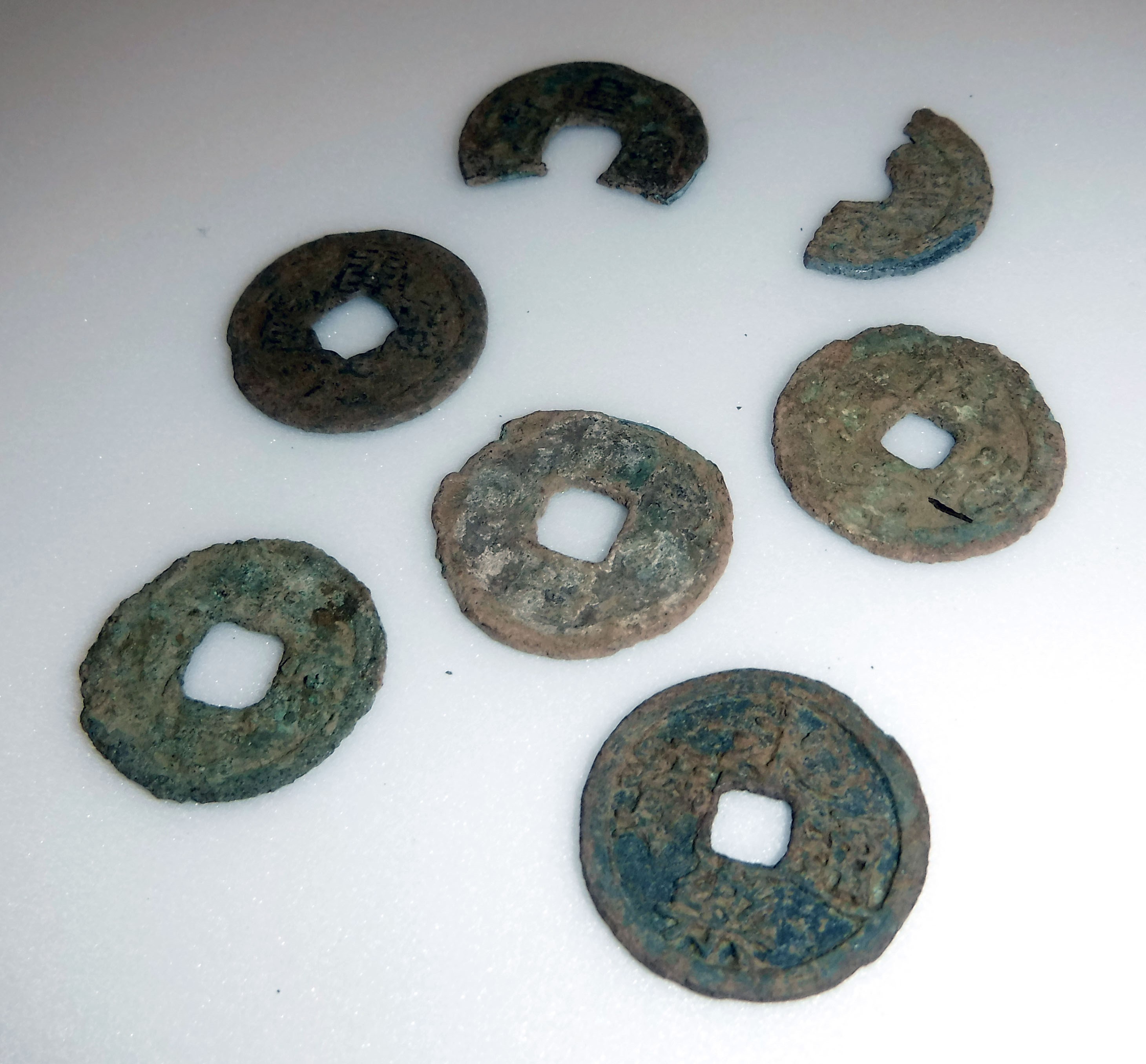 養郷宮之脇遺跡で出土した古銭７枚が写っている写真です。５枚はほぼ完全な形ですが、２枚は半分近くがかけています。表面には緑錆がついています。